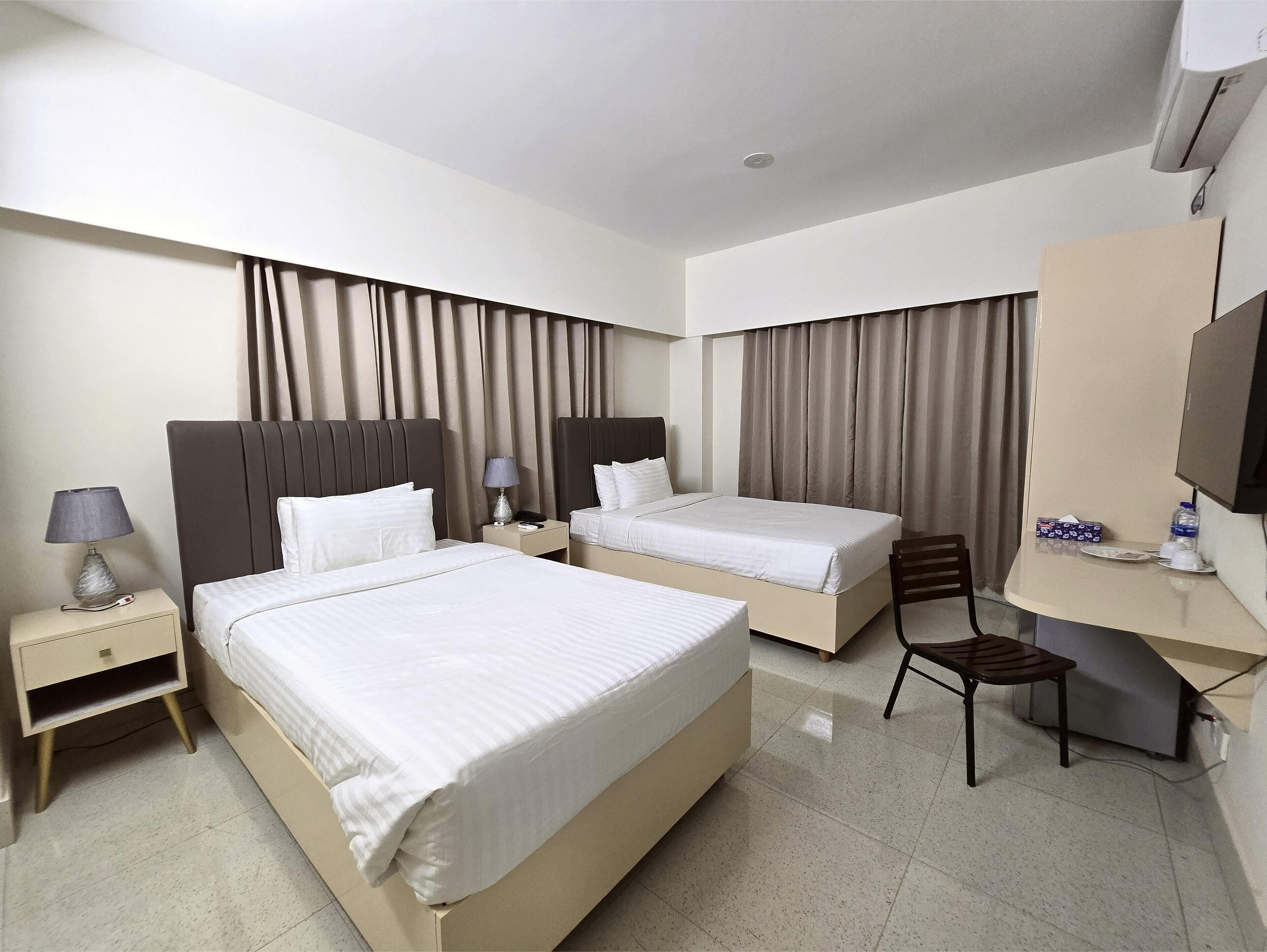A hotel room with two beds, a desk, a chair, a TV, and curtains.