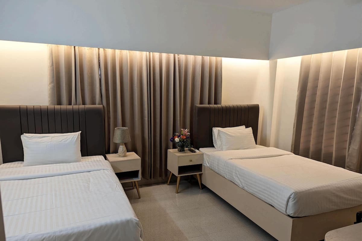 A hotel room with two beds, a nightstand with a lamp, and a small table with a vase of flowers.