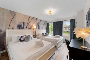 A hotel room with two beds, a desk, a chair, a lamp, and a view of the outdoors. - 4 Apartments, 10BR - Two and a Half Miles to Ark! (Williamstown)
