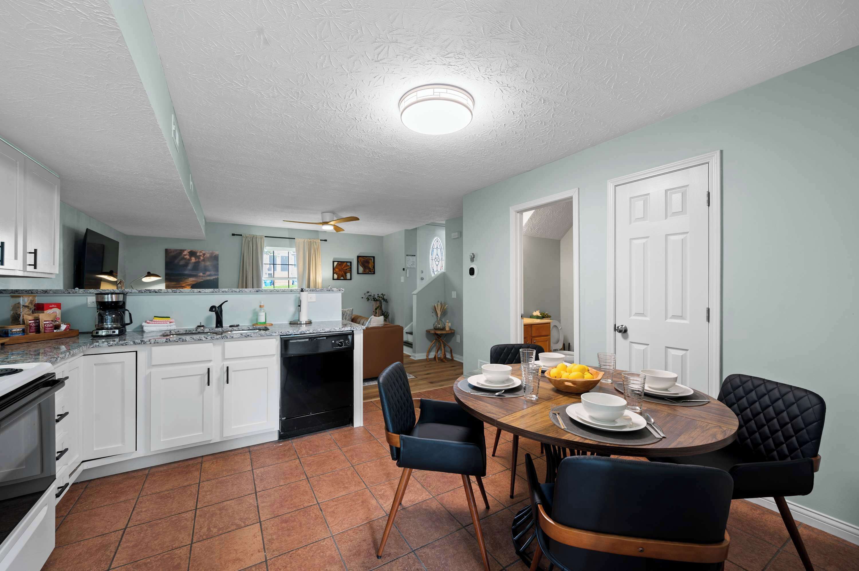 A modern kitchen with white cabinets, a dining area with a wooden table and black chairs, and a ceiling fan.