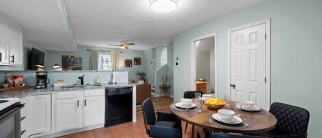 A modern kitchen with white cabinets, a dining area with a wooden table and black chairs, and a ceiling fan.