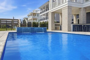 A swimming pool with a tiled waterfall feature, surrounded by a brick pool deck and a fence.