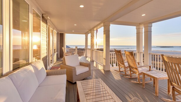 A covered outdoor area with a white sofa, wicker chairs, and a wooden table. - Freedom  Point: Oceanfront Luxury w/Pool, Game Room, Sauna & Cold Plung (Garden City Beach)