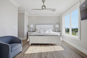 A bedroom with a bed, nightstands, a ceiling fan, a large window, and a view of the outdoors.
