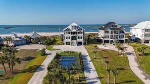 A beachfront property with multiple houses, a tennis court, and a view of the ocean.