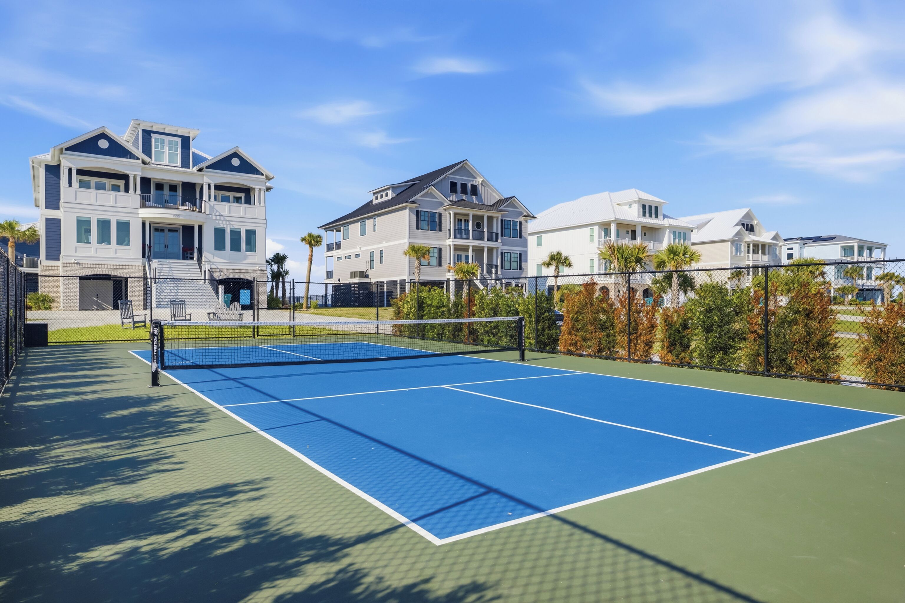 A tennis court with a net, surrounded by a fence, and adjacent to a multi-story residential building.
