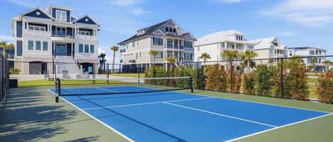 A tennis court with a net, surrounded by a fence, and adjacent to a multi-story residential building.