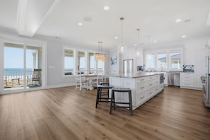 A modern kitchen with a large island, white cabinetry, and a view to the outside. - Freedom  Point: Oceanfront Luxury w/Pool, Game Room, Sauna & Cold Plung (Garden City Beach)