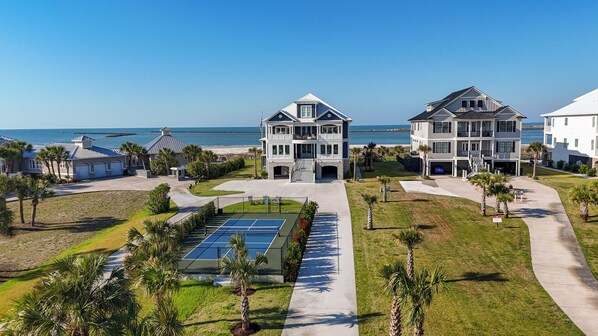 A beachfront property with a tennis court, multiple buildings, and a view of the ocean.