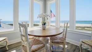 A room with a round table, white chairs, a vase with flowers, and an American flag. - Freedom  Point: Oceanfront Luxury w/Pool, Game Room, Sauna & Cold Plung (Garden City Beach)