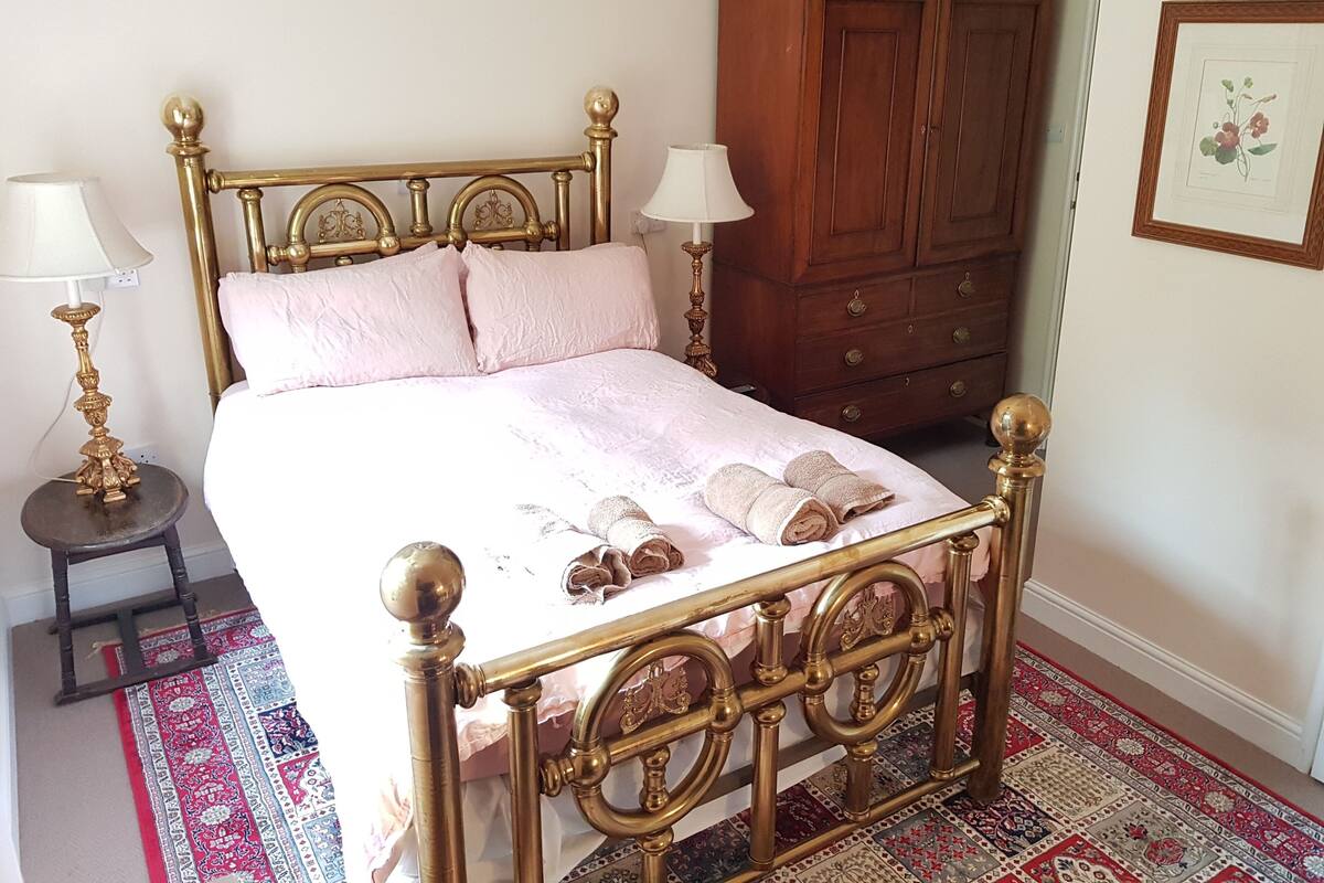A bedroom with a four-poster bed, a wooden wardrobe, and a patterned rug.