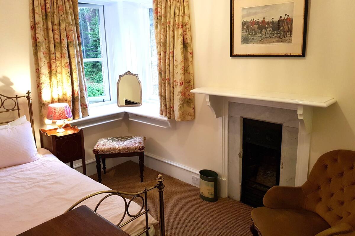 A bedroom with a bed, a nightstand, a chair, a fireplace, and a window with curtains.