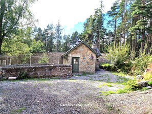 Ein Steinhaus mit einer grünen Tür, umgeben von einem Kiesweg und dichtem Wald.