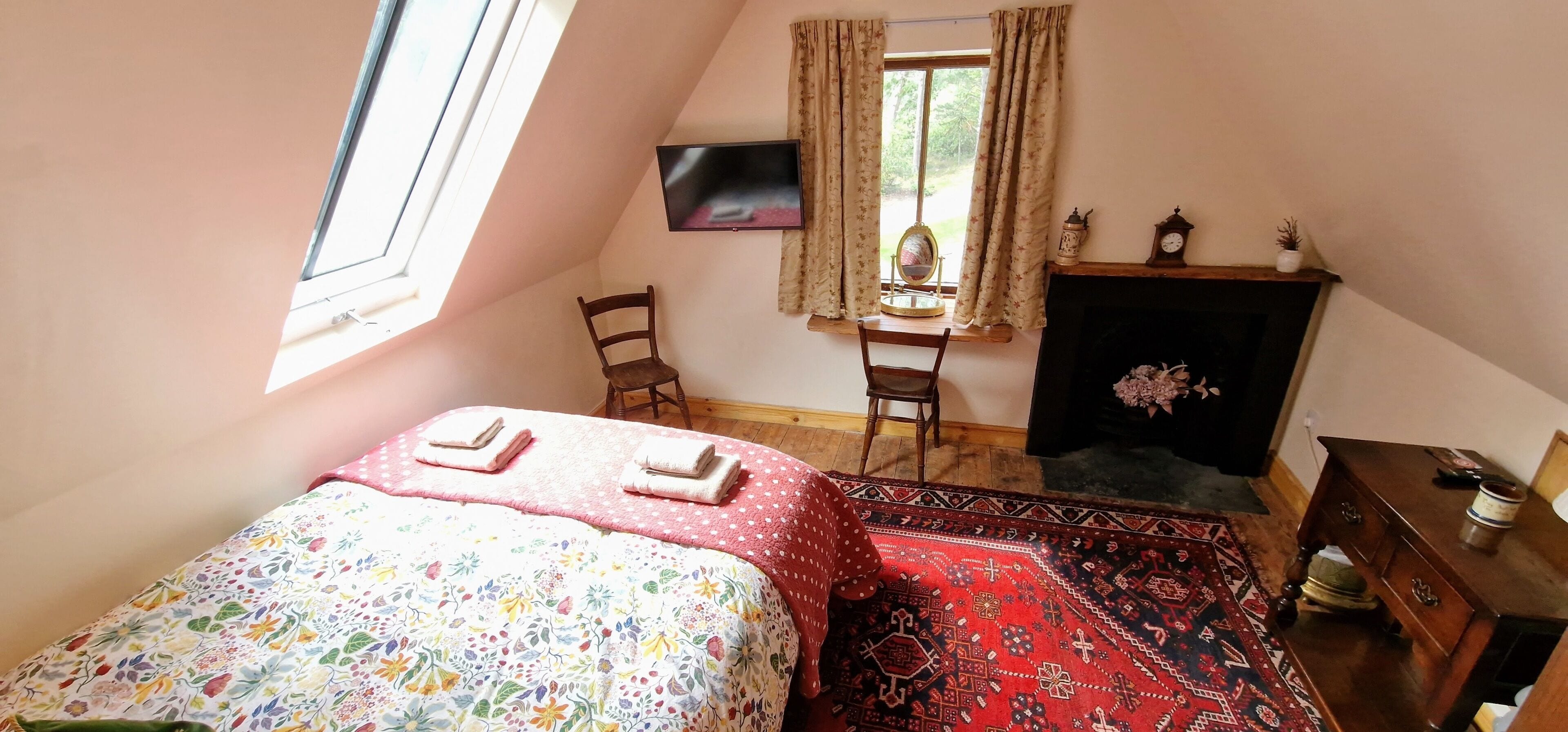 Un dormitorio con cama, una silla, un escritorio, chimenea y ventana.