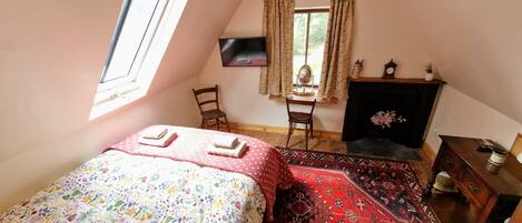 Un dormitorio con cama, una silla, un escritorio, chimenea y ventana.