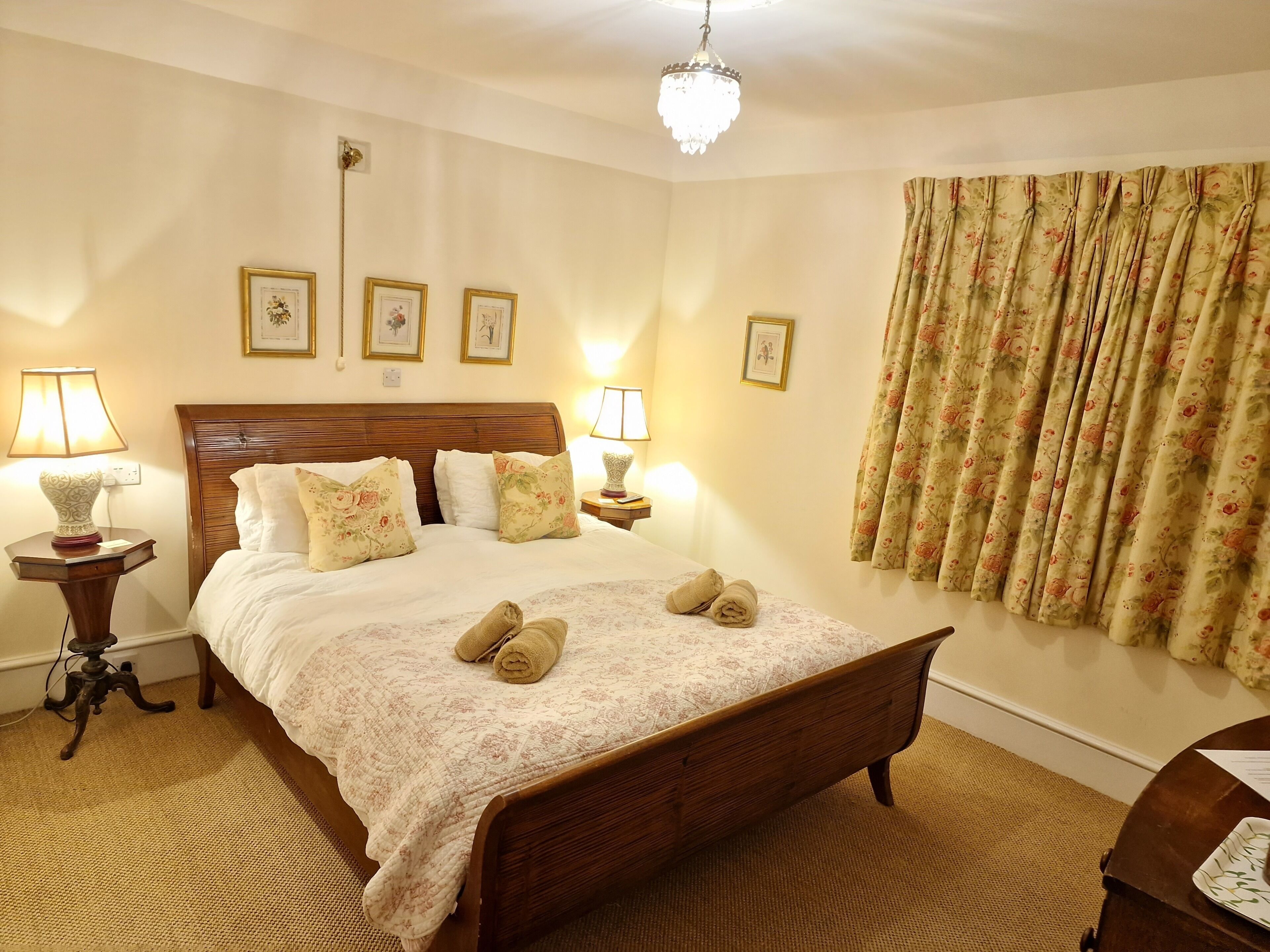 A neatly made bed with floral bedding, two bedside lamps, and a chandelier.