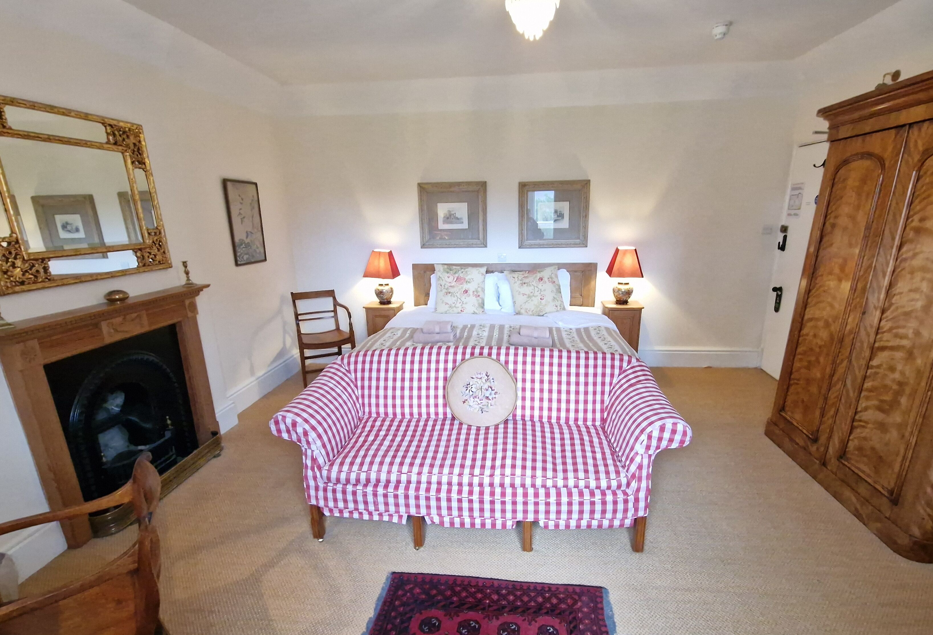 Une chambre à coucher avec une couvre-lit à carreaux, une armoire en bois, une cheminée et des tableaux encadrés accrochés au mur.