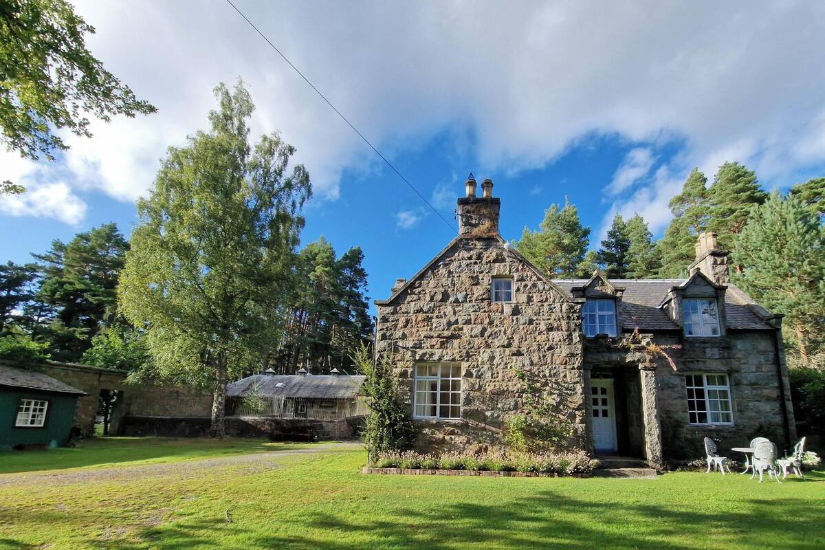 A stone house with a traditional design, featuring a stone chimney, multiple windows, and a well-maintained lawn.