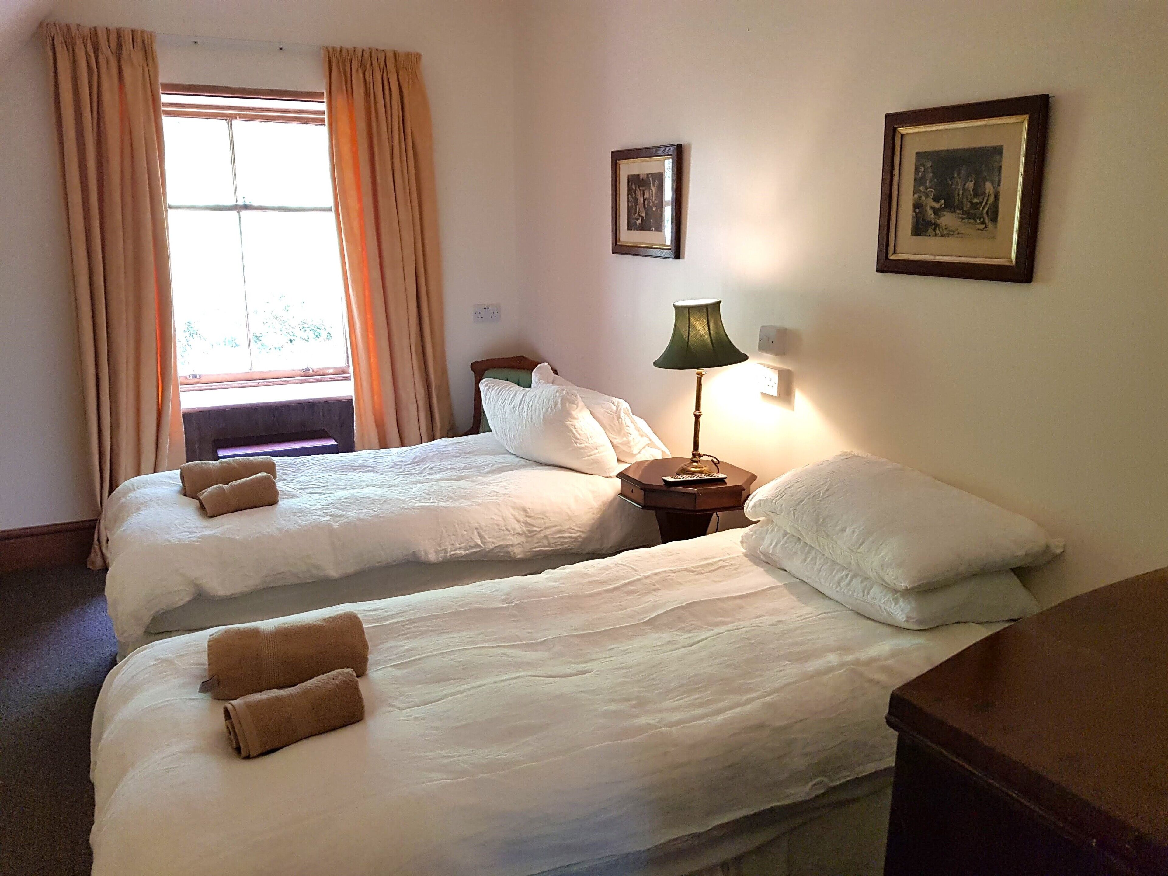 Une chambre d’hôtel avec deux lits, une table de chevet avec une lampe et une fenêtre avec des rideaux.