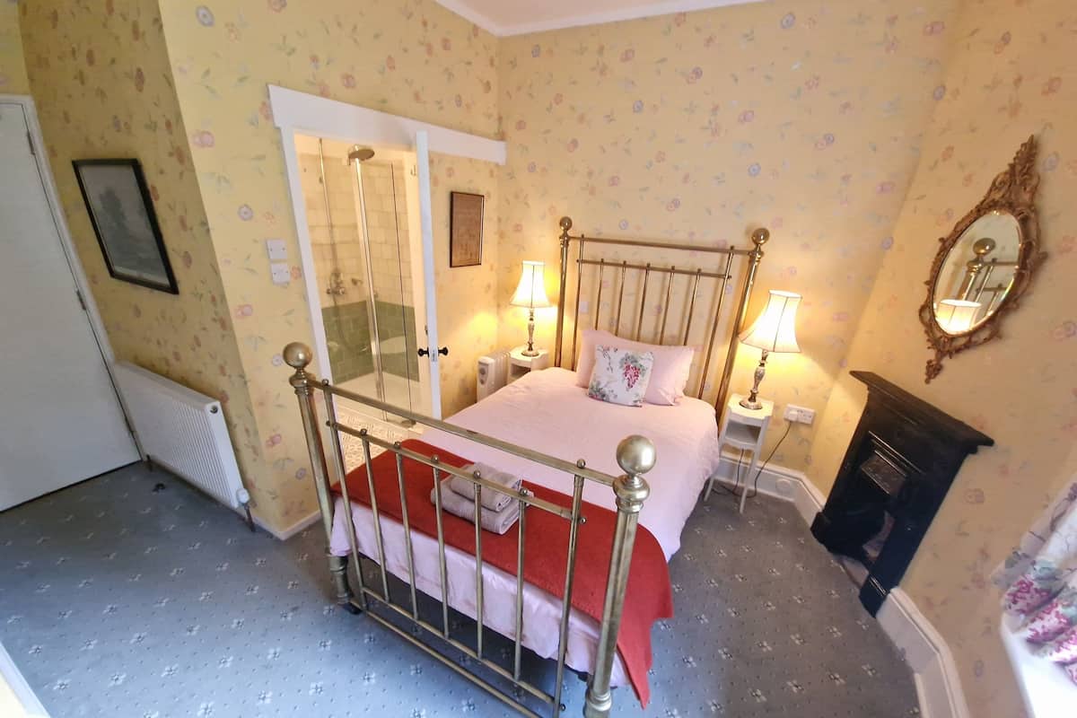 A bedroom with a bed, two bedside tables with lamps, a mirror, a radiator, and a fireplace.