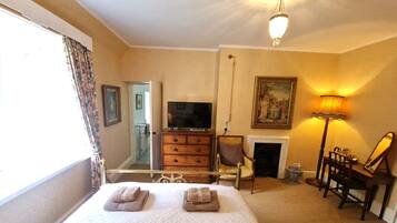 A hotel room with a bed, a television, a fireplace, a desk with a lamp, and a chair.
