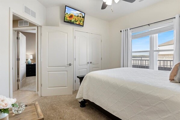 A bedroom with a bed, a television, a ceiling fan, and a window with curtains.