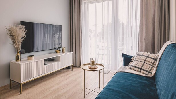 A modern living room with a large flat-screen TV, a white console table, a blue sofa, and a small round coffee table. - Linterna Luksus nad Ba Tykiem Let s Sea G ski SPA (Mielno)