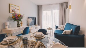 A modern living room with a blue sofa, a dining table set for four, and a TV on a white cabinet. - Linterna Luksus nad Ba Tykiem Let s Sea G ski SPA (Mielno)