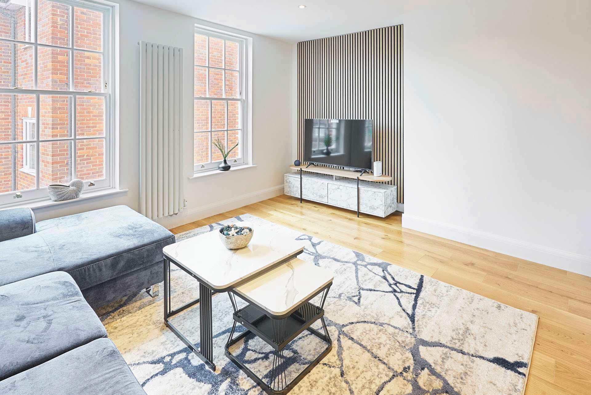 A modern living room with a sofa, a coffee table, a TV, and a patterned rug.