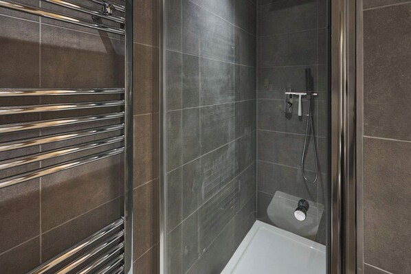 Un bagno moderno con cabina doccia in vetro, pareti piastrellate scure e un porta asciugamani cromato.