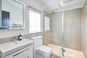 Features a large mirror, sink, toilet, and glass-enclosed shower with handheld showerhead.