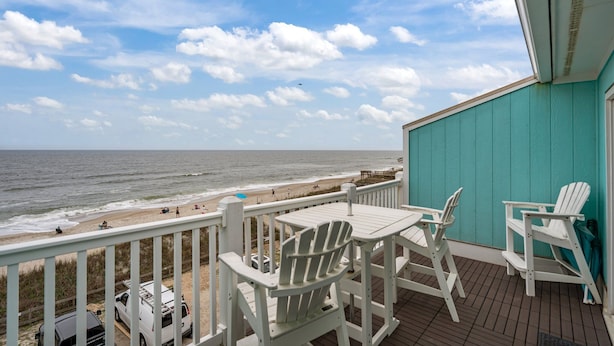 A deck with white Adirondack chairs and a table overlooking a beach with people and vehicles. - Top Floor 2 Bdrm/2 Bath OCEAN FRONT,BEACH ACCESS condo.  Sleeps 6 with Linens! (Carolina Beach)