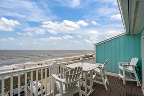 A deck with white Adirondack chairs and a table overlooking a beach with people and vehicles. - Top Floor 2 Bdrm/2 Bath OCEAN FRONT,BEACH ACCESS condo.  Sleeps 6 with Linens! (Carolina Beach)