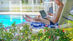 Een man zit aan een zwembadstoel en gebruikt een laptop.