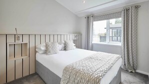 A bedroom with a bed, a bedside table, a window with curtains, and a view of the outside.