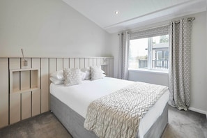 A bedroom with a bed, a headboard, a window with curtains, and a view of the outside.