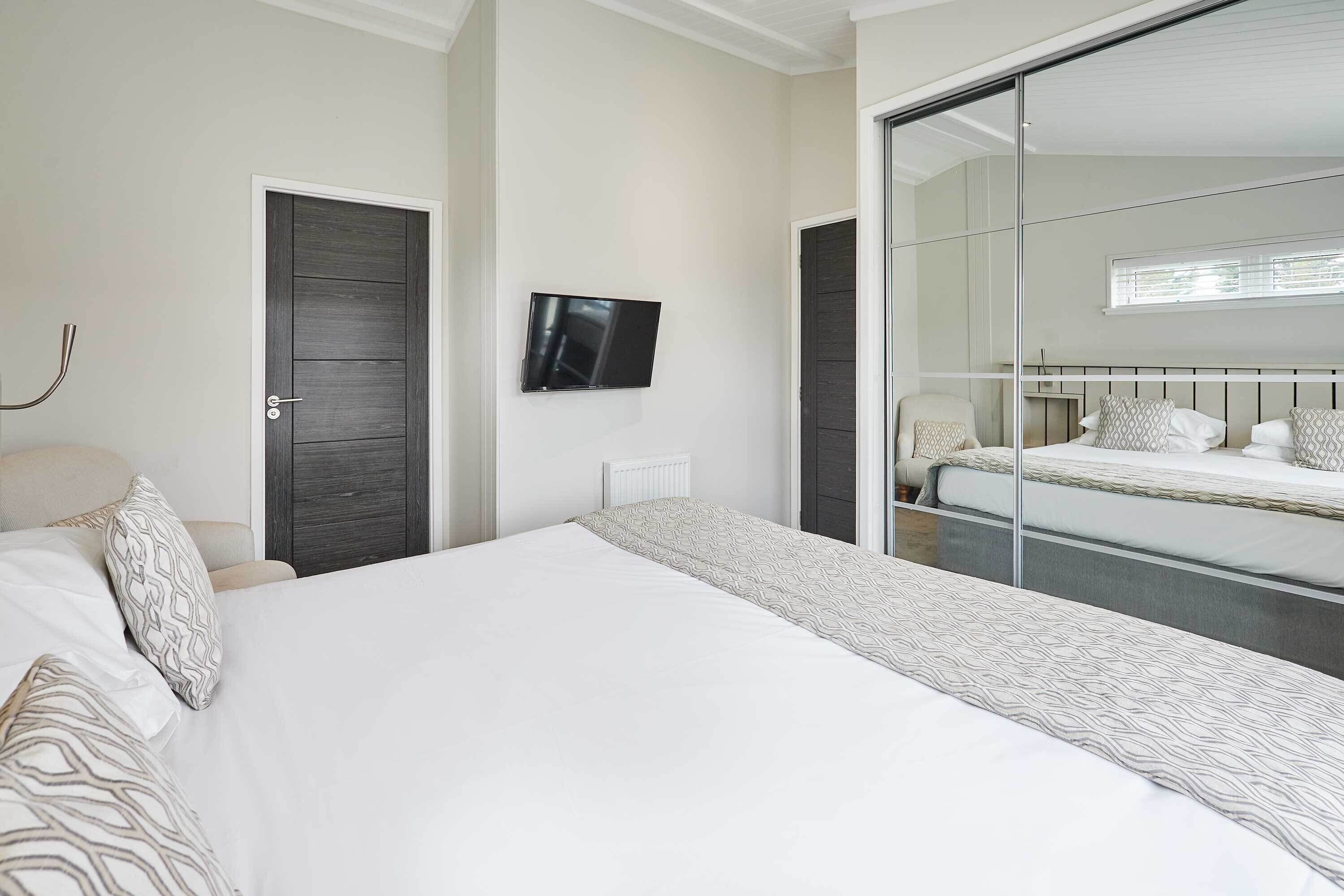 A bedroom with a large bed, a television mounted on the wall, and a sliding door leading to another room.