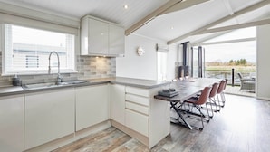 A modern kitchen with white cabinets, a large island with bar stools, a built-in oven, and a view through large windows to the outdoors.