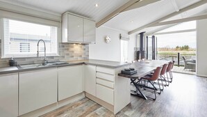 A modern kitchen with white cabinets, a large island with bar stools, a built-in oven, and a view through large windows to the outdoors.