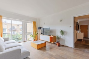 Ein modernes Wohnzimmer mit einer Couch, einem Couchtisch, einem Fernseher und einer Topfpflanze.