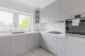Uma cozinha moderna com armários brancos, forno Bosch, fogão a gás e janela com vista para edifícios e árvores.