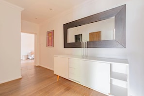 Um corredor com um console branco, um espelho grande e piso de madeira.