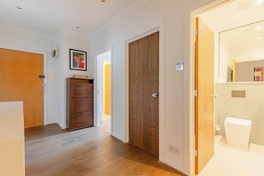 Ein Flur mit Holzboden, einem Holzschrank, einer Holztür und einem Badezimmer mit weißer Toilette und gefliesten Wänden.