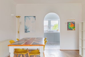 Ein Essbereich mit Tisch, der ein Union-Jack-Design aufweist, gelben Stühlen und einer modernen Pendelleuchte.