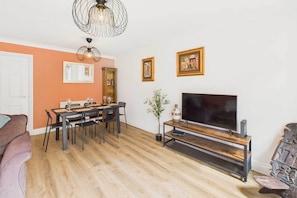 A living room with a dining area, a TV on a wooden stand, and a plant.