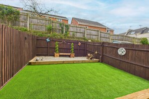 A backyard with artificial grass, a wooden deck, and a wooden fence.