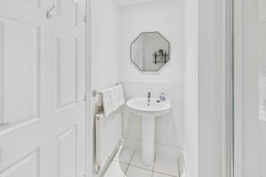 Un baño con paredes blancas, un lavabo blanco, un espejo y una toalla colgada en el radiador.