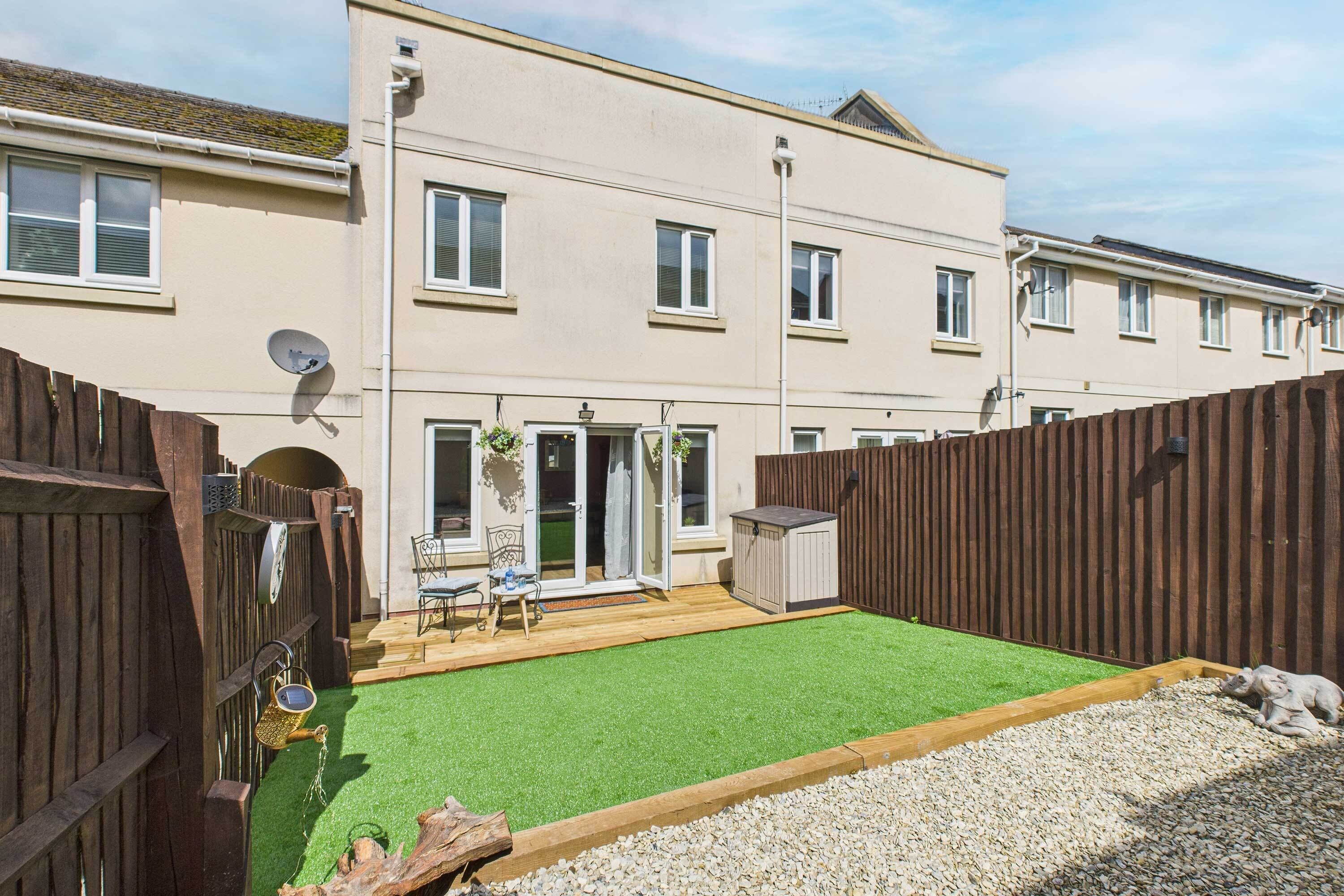 A two-story residential building with a fenced backyard, a wooden deck, and a small shed.
