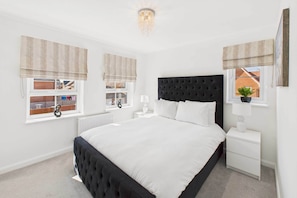 A bedroom with a large bed, two bedside tables, a window with blinds, a radiator, and a ceiling light fixture. - Host & Stay | Orient House (Yarm)