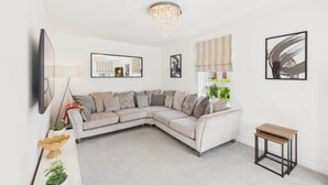A modern living room with a sectional sofa, a small side table, and a large mirror. - Host & Stay | Orient House (Yarm)